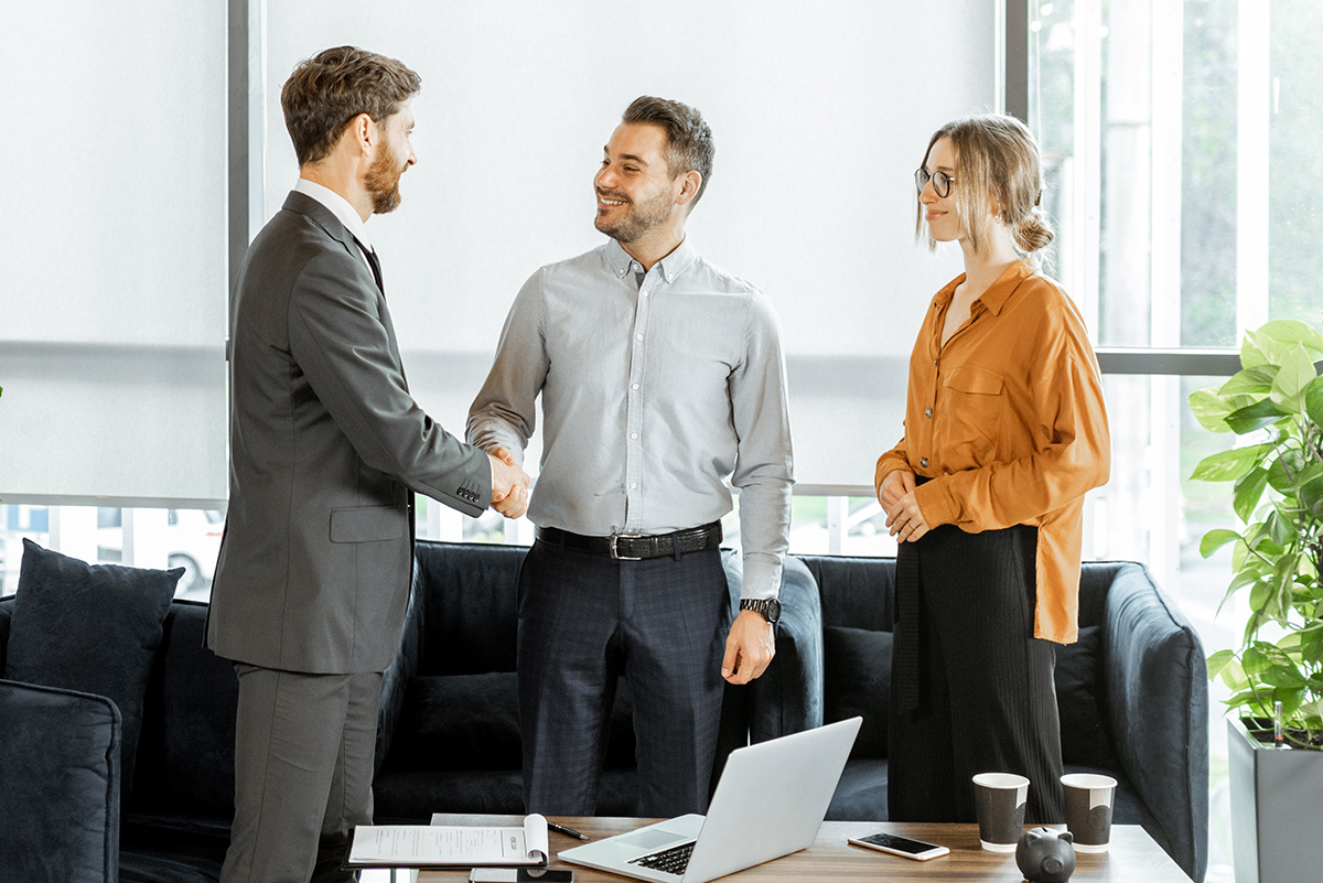 Young and happy couple having a deal, shaking hands with financial consultant or real estate agent at the luxury office